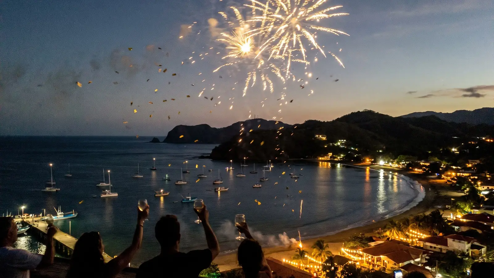Fuegos artificiales sobre la bahía al anochecer, con copas en alto en primer plano