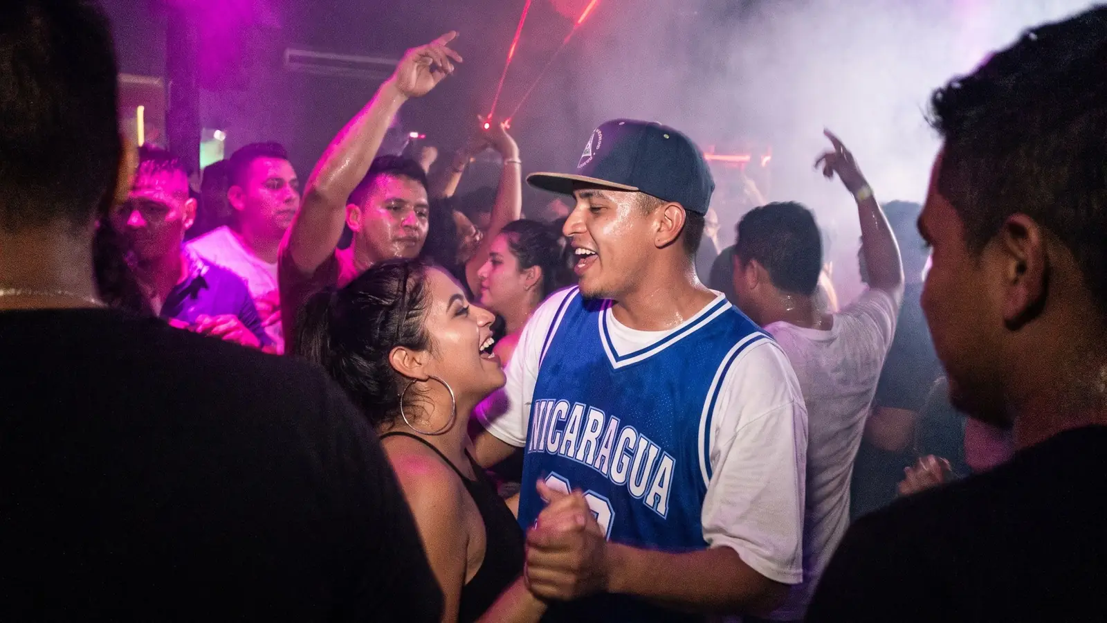 Pareja bailando en una pista llena, entre humo y luces violetas